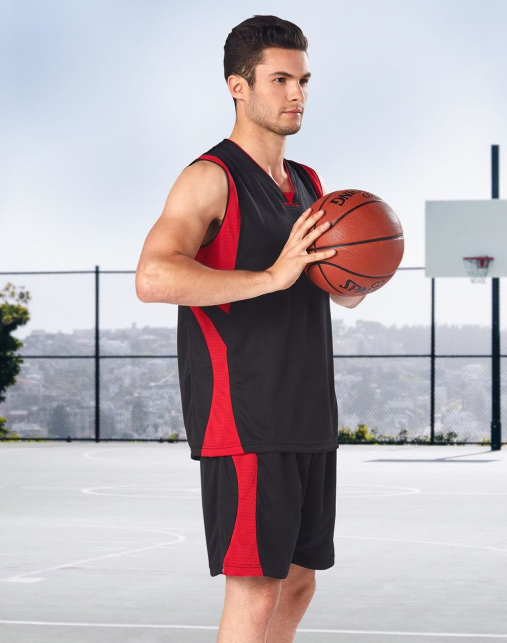 Adults' basketball shorts in black with red accents, showcased by a model holding a basketball on a court.