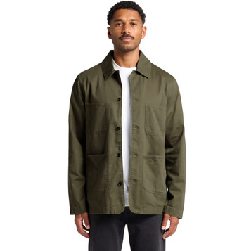 A man wearing an olive green Chore Jacket with multiple pockets and a logo. The jacket has a classic collar and button front.