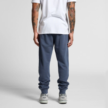 Premium track pants in a dark blue colour, featuring a fitted design and elasticized cuffs. The model is wearing a white shirt.