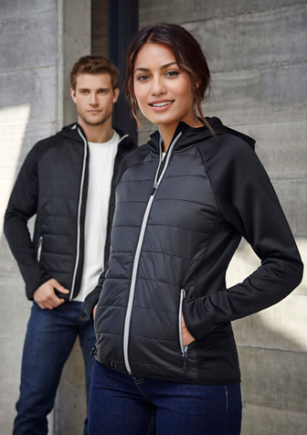 A woman models a black puffer jacket with a zip, featuring a hood and contrasting details. A man stands behind her in a white shirt.