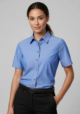 A short-sleeve chambray button-up shirt in blue with a chest pocket, modelled by a woman.