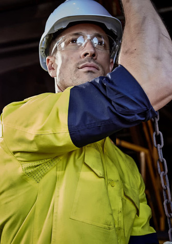 A rugged long sleeve shirt in yellow and navy, featuring reflective elements and a logo, worn by a person in safety gear.