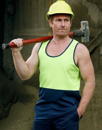 A man wearing a hi-vis yellow and navy safety singlet, holding a hammer over his shoulder, with a hard hat on.