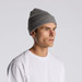 A grey knit beanie worn by a model, featuring a ribbed texture, against a plain background.