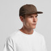 A cap in a muted brown colour worn by a model, featuring a simple design and a logo.