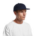 A navy Class Wool Cap with a flat brim, worn by a model in a white t-shirt. The cap features a logo.