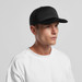 A black trucker cap with a mesh back, worn by a model in a white t-shirt. Features a logo on the front.