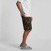 A pair of camouflage shorts in green and brown tones, with a side pocket, worn with a casual white t-shirt.