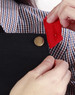 A black canvas bib apron is being adjusted, showcasing a button detail and a red fabric tag.