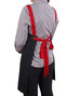 A black canvas bib apron with red straps tied at the back, worn by a person in a checkered shirt.