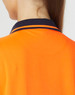 A close-up of a bright orange polo shirt with a navy collar and stripes, featuring a logo.