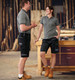 Unisex utility stretch cargo work shorts in black, paired with grey tops, alongside two models in a workshop setting.