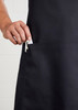 A black bib apron with a hand inserting a clip into a pocket, featuring a logo.