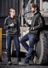A pair of people wearing black hoodies and blue stretch denim work jeans, standing beside a large vehicle tire.
