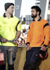 Two men wearing short-sleeve polo shirts in bright yellow and orange, featuring logos and workwear-style designs.
