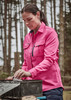 A long sleeve women's button-up shirt in pink, featuring chest pockets, worn outdoors among trees.