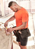 A men's high visibility t-shirt in bright orange, worn by a tradesman measuring wood, with a tool belt.