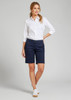 A woman in a white shirt and navy chino shorts stands against a grey background. The shorts feature a logo.