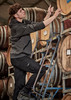 A person in a dark grey unisex water-resistant hoodie climbing a ladder among wine barrels. The hoodie has a logo.