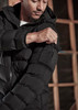 A black unisex puffer jacket with a hood, featuring a zip-up front and a pocket on the arm.