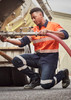 A worker in orange and navy striped attire kneels beside a tanker, wearing Mens Bio Motion Taped Stretch Jeans.