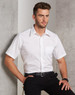 A white short sleeve button-up shirt with a pocket, featuring a logo, worn by a model against a textured background.