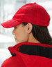 A red athletic mesh cap with a curved brim, featuring a logo, worn by a model from the side.
