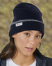 A navy beanie with a grey band and a logo, worn by a person with long hair in a blurred outdoor background.