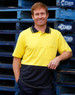 A man in a yellow and navy two-tone safety polo shirt stands beside blue pallets. The shirt features a pocket and a logo.