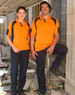 Men and woman in high-visibility orange polo shirts with navy sleeves, standing in a construction setting. 