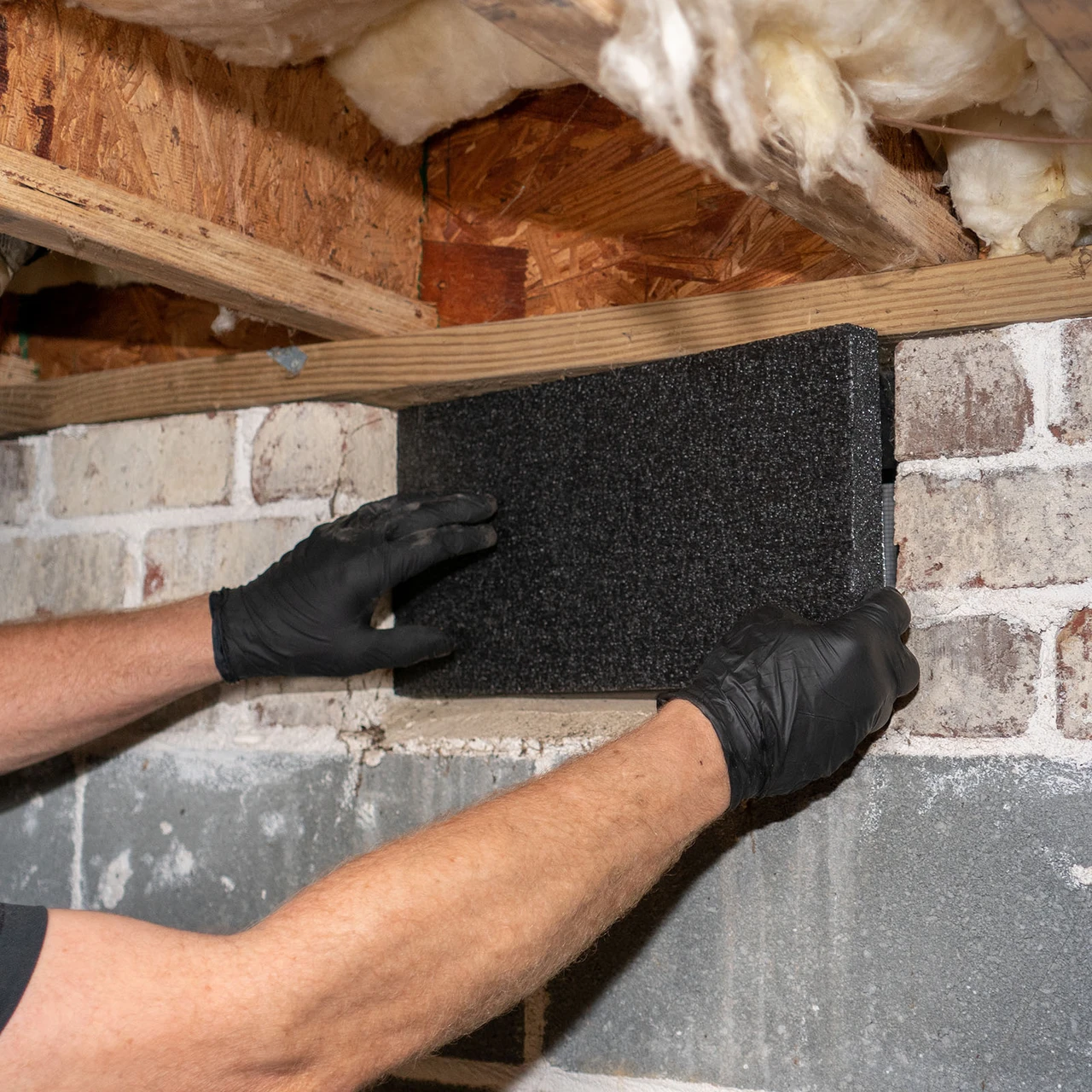 Press-fitting VentBlock+ into the back of a foundation vent from inside the crawl space