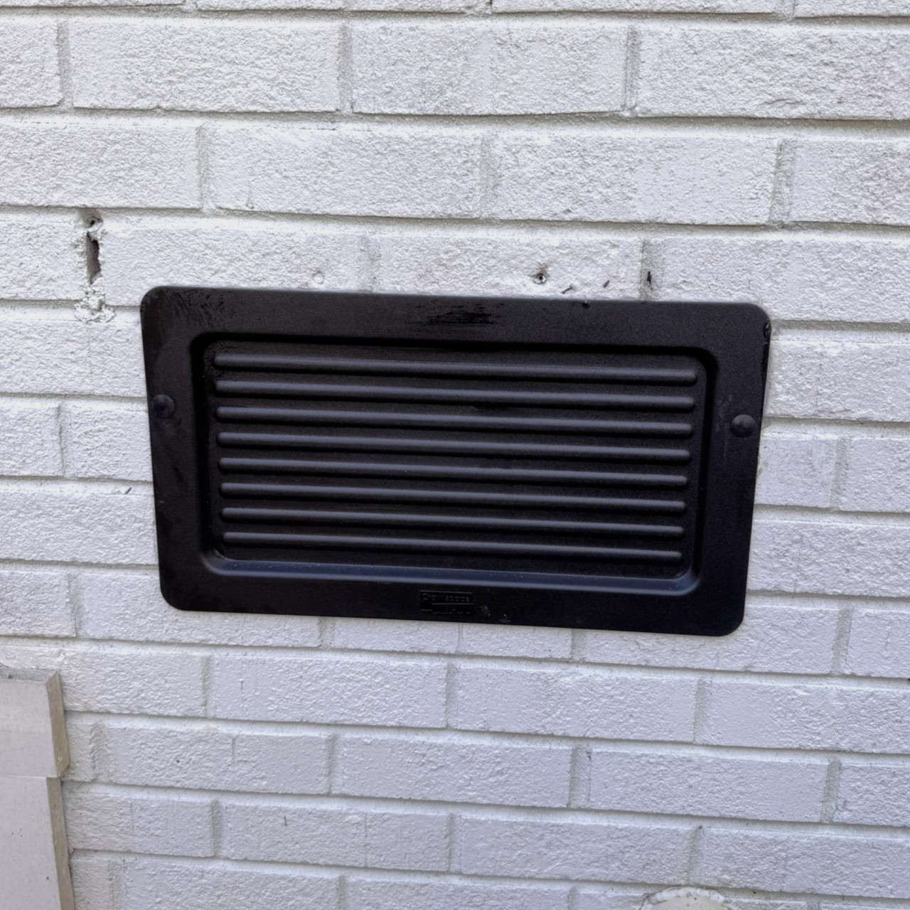 Exterior foundation vent cover installed over an existing vent opening on a brick foundation wall, sealing the vent from outside the home