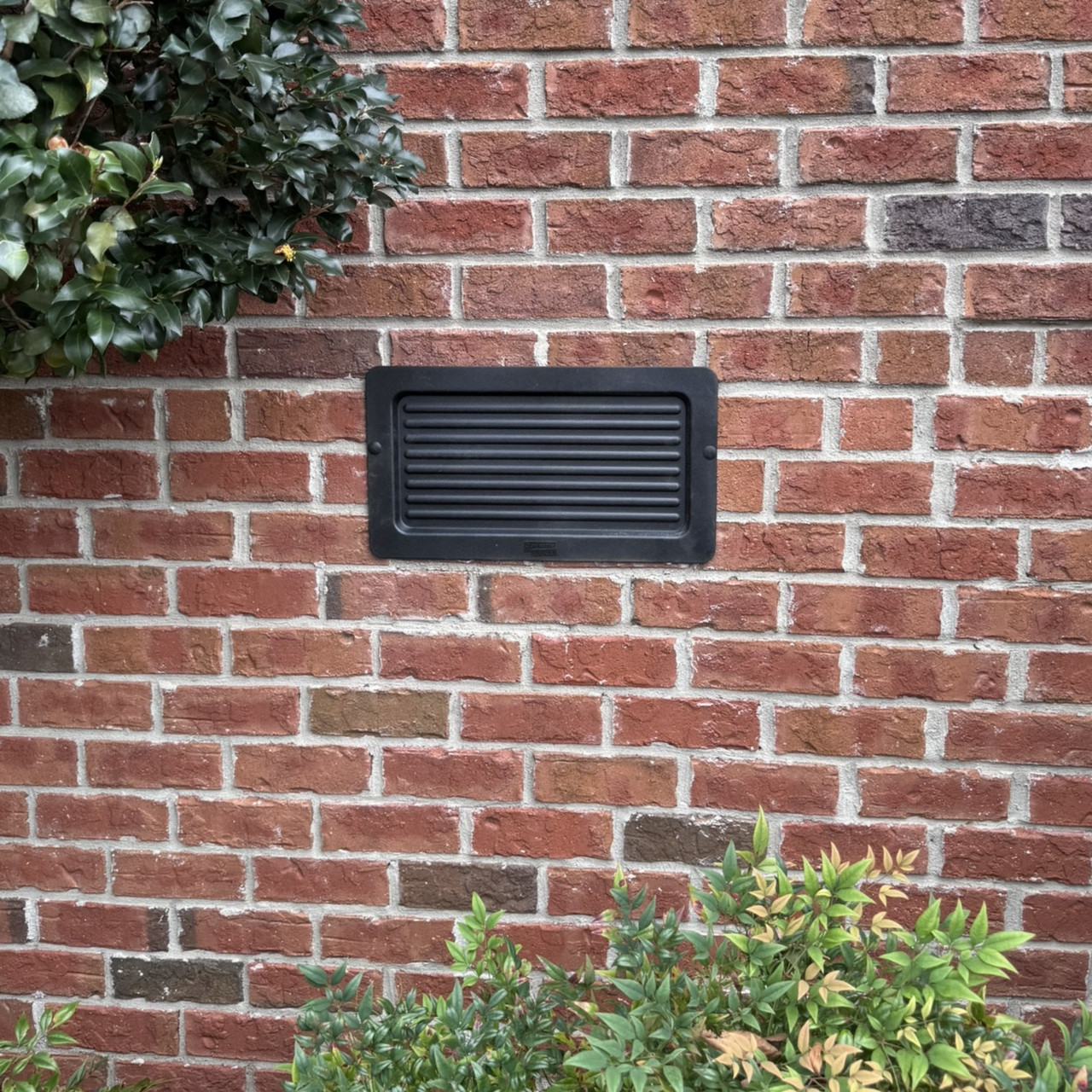 Exterior foundation vent cover installed on a brick foundation wall, sealing an existing vent opening from the outside of the home