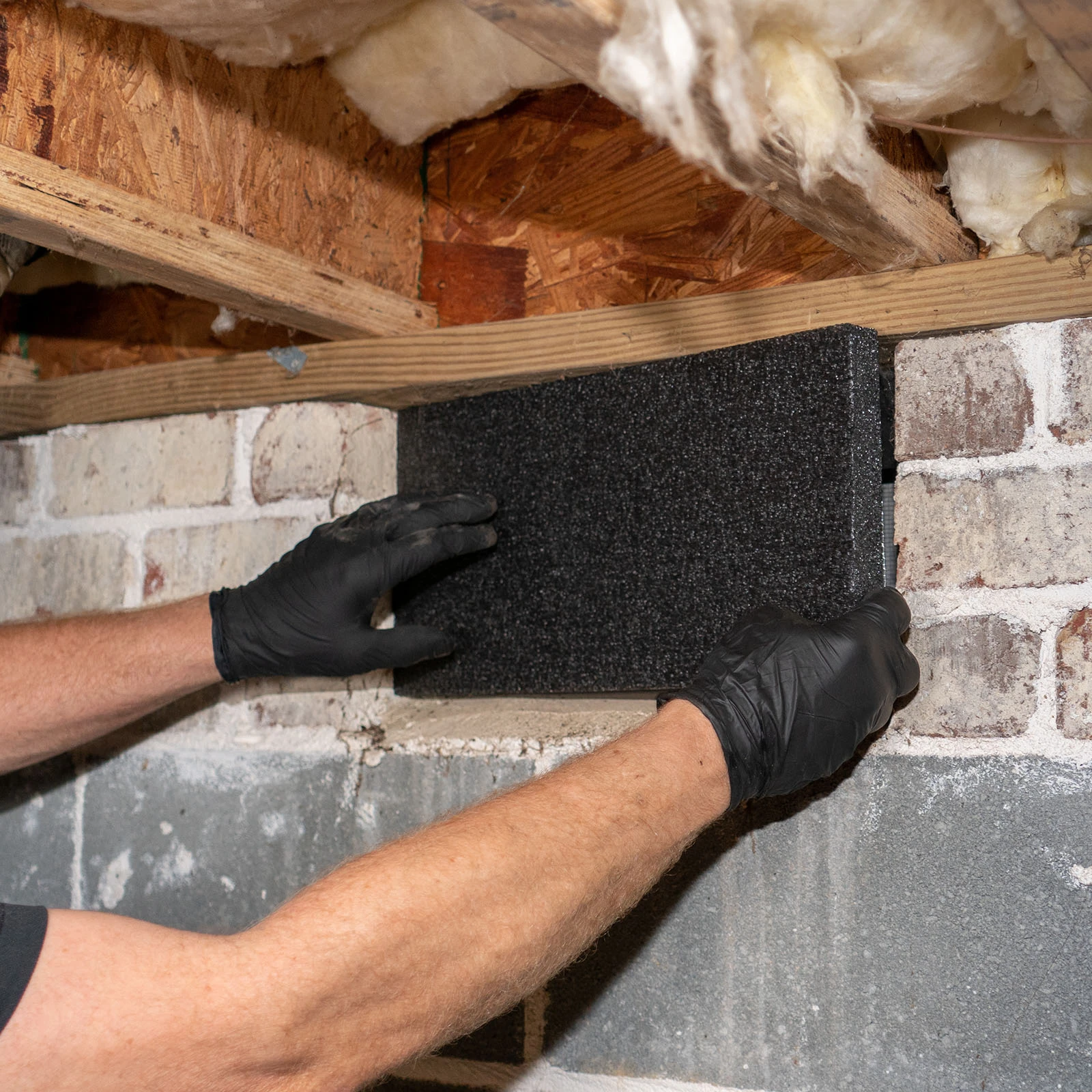 Press-fitting VentBlock+ into the back of a foundation vent from inside the crawl space