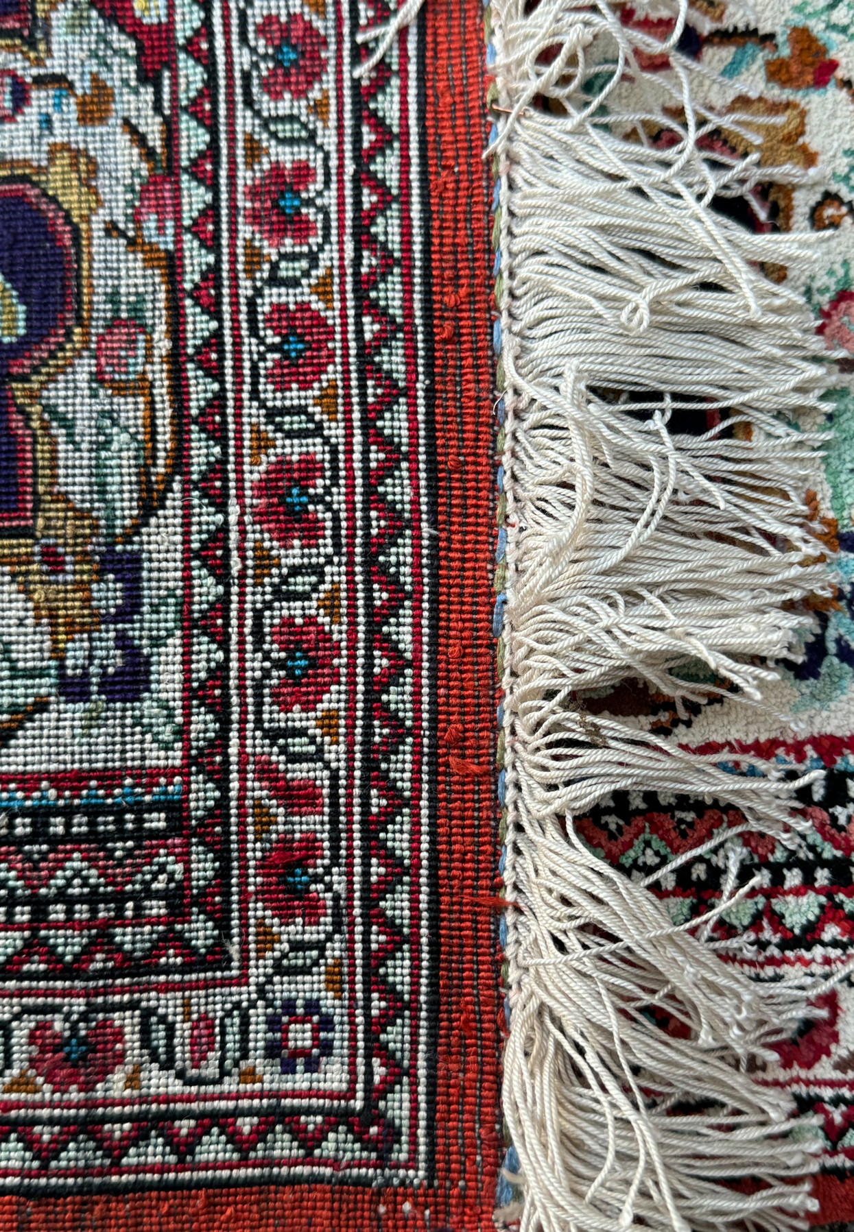 Partial view of a Persian Qum silk rug with a focus on the detailed floral border and fringe