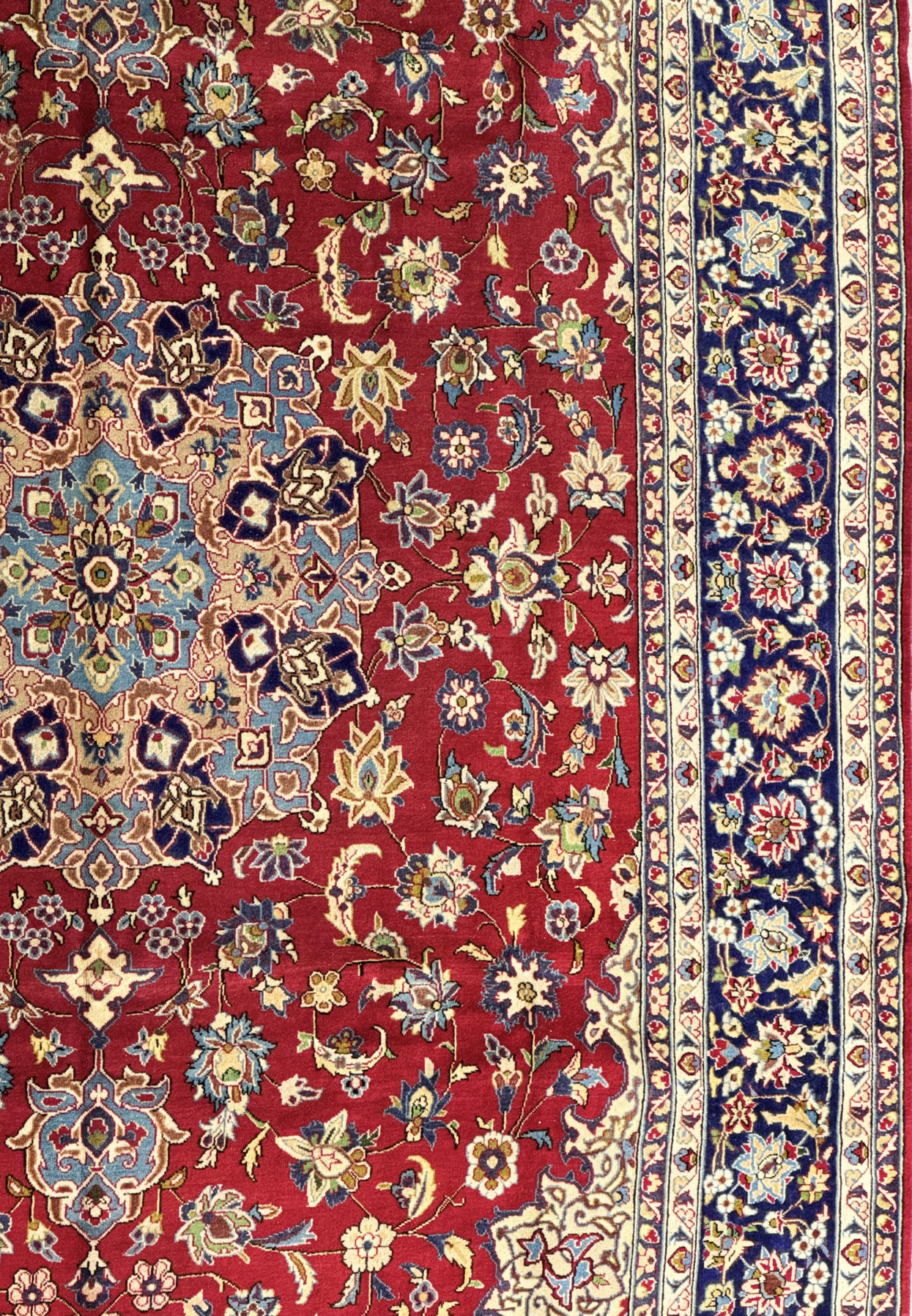 Partial view of a 10 x 15 Persian Isfahan rug laid out to display the harmonious design with a deep crimson field and a navy blue border rich with floral patterns