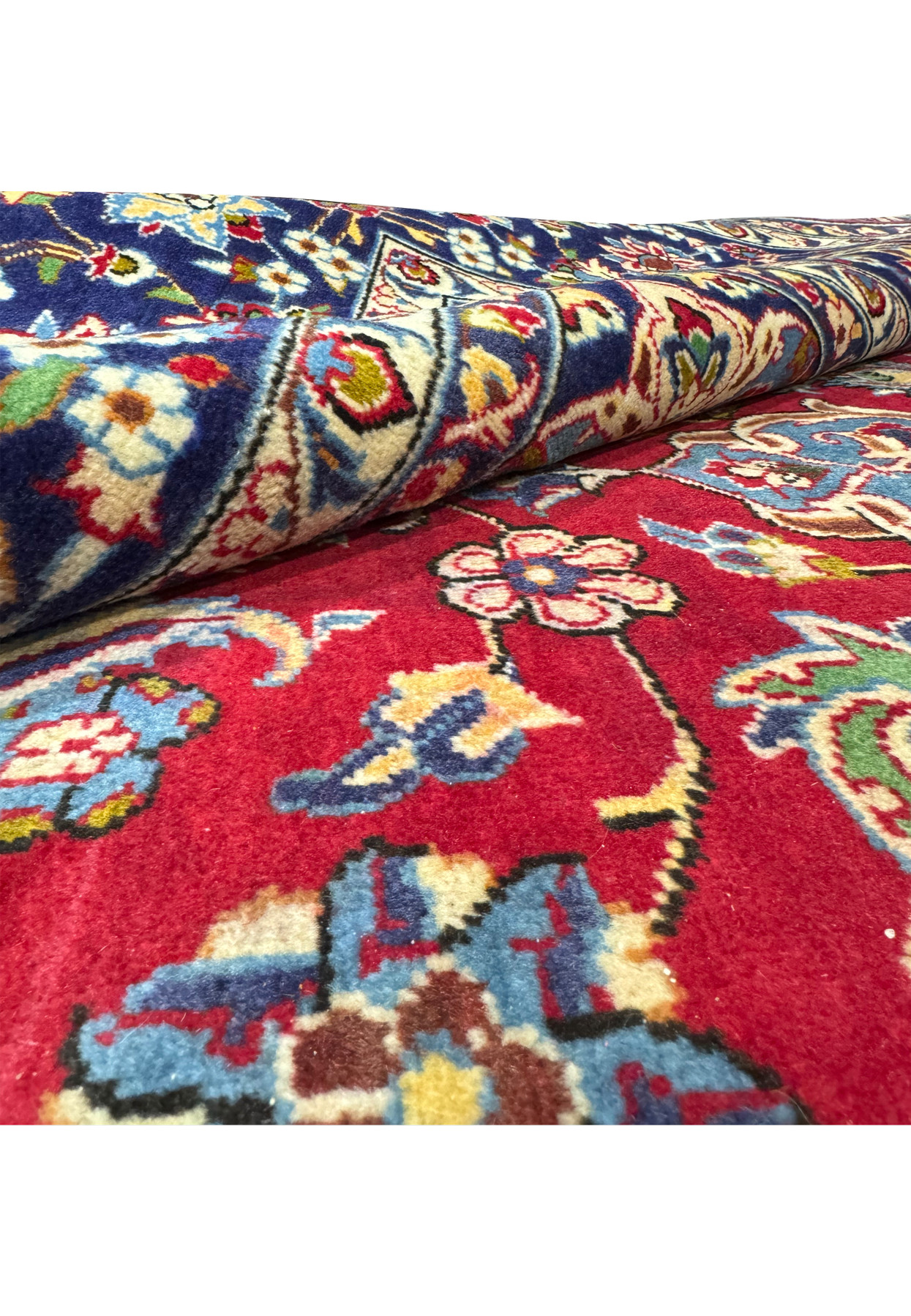 A 10 x 15'6" Persian Isfahan rug partially rolled, displaying the detailed patterns and vivid colors on the intricate border and the plush red field