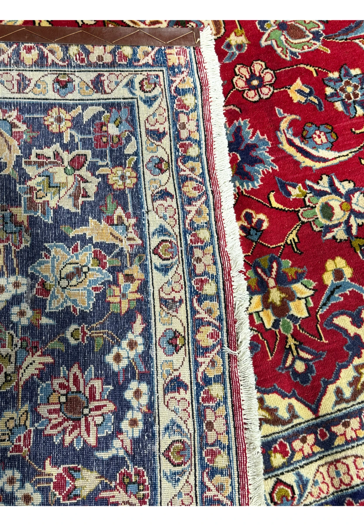 A close-up edge view of a 10 x 15'6" Persian Isfahan rug, emphasizing the detailed border and the back of the rug showing the amazing weaving technique with deep navy blue and vibrant floral patterns on a cream background