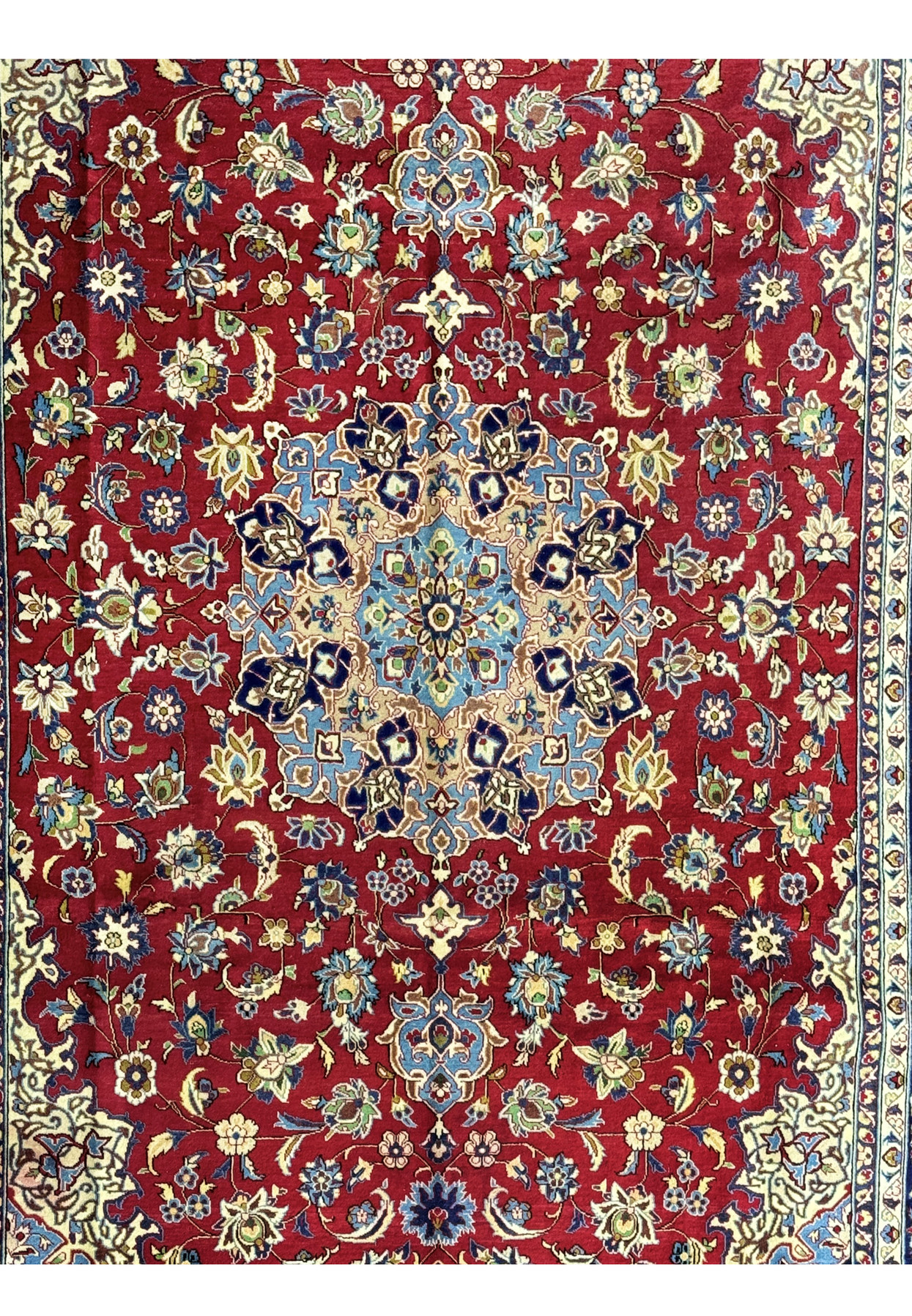 An angled view of the Persian Isfahan rug, highlighting the texture and sheen of the woven fibers and the rich color contrast between the red field, the blue border, and the delicate floral motifs