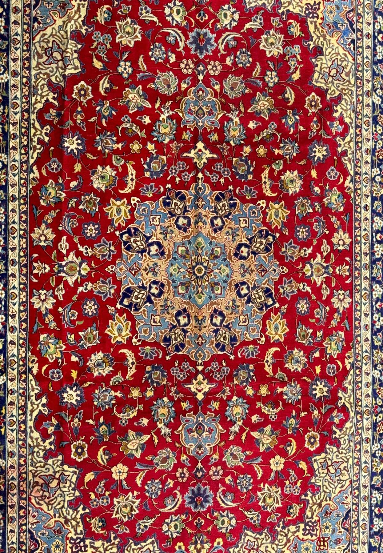 A close-up view of the central part of a Persian Isfahan rug, highlighting the elaborate central medallion and the detailed floral patterns in colors of blue, gold, and white on a red background