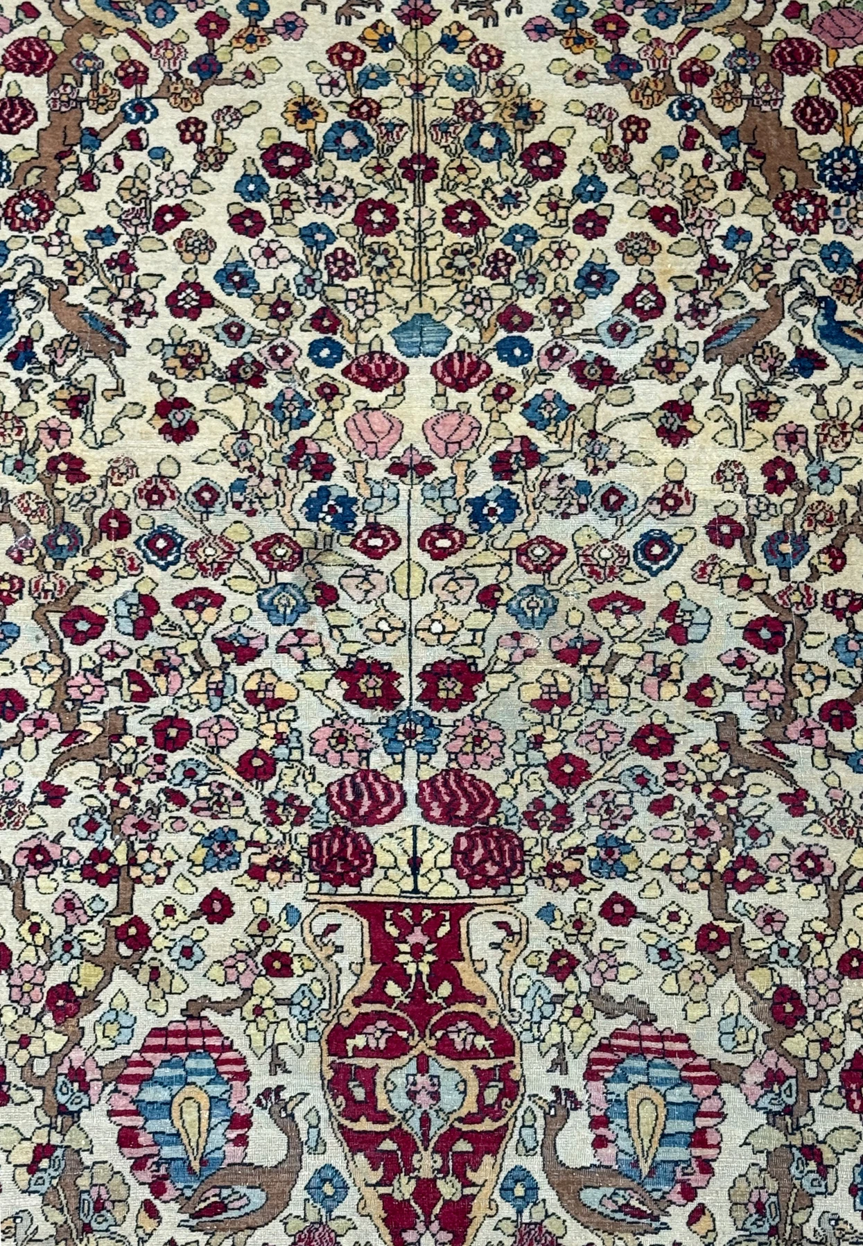 A close-up of the central part of the rug, highlighting the detailed vases and tree of life motif amidst the floral patterns.