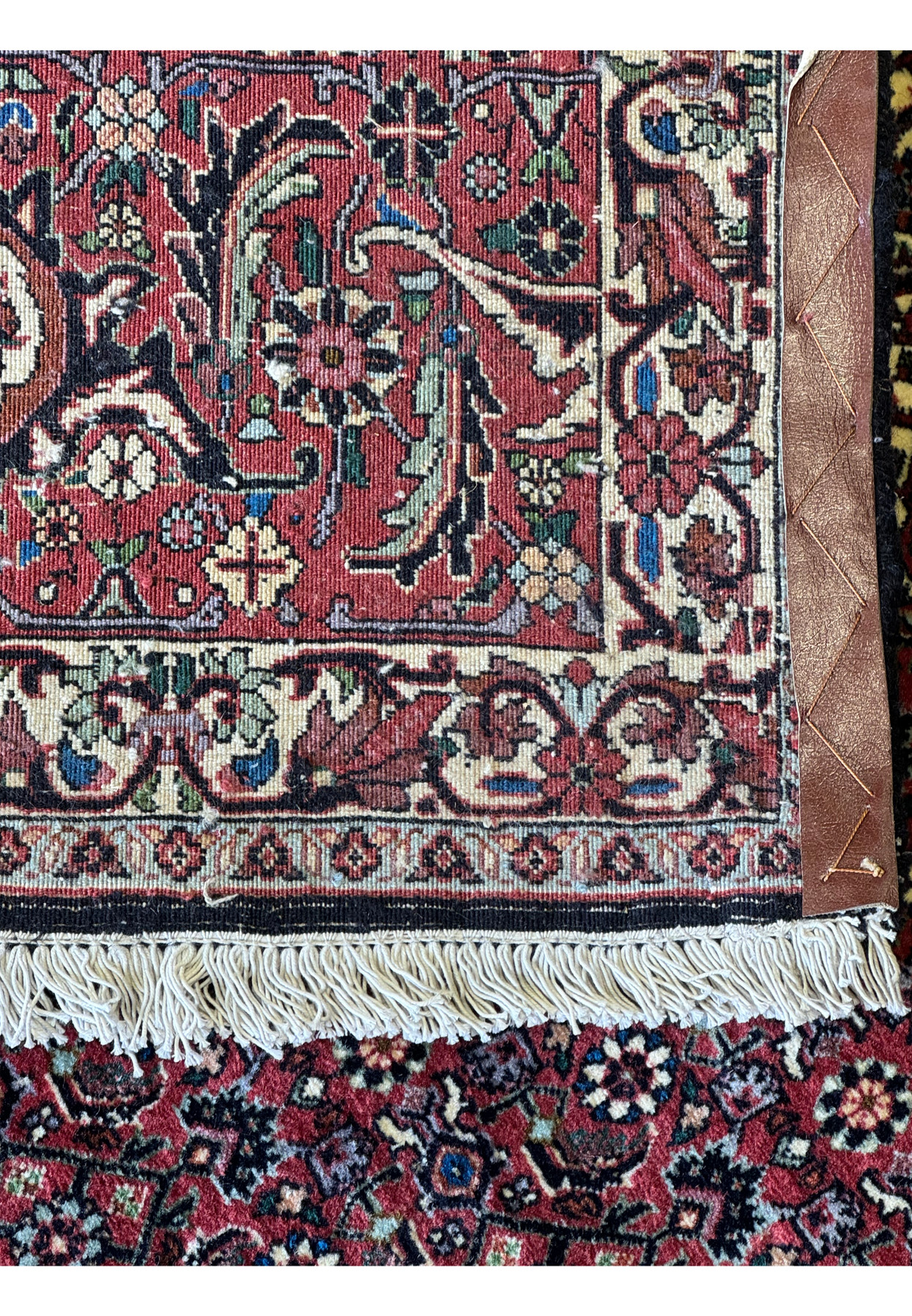 The fringe of a Persian Bidjar rug, with a glimpse of the elaborate border patterns and the rich, deep coloration of the weave