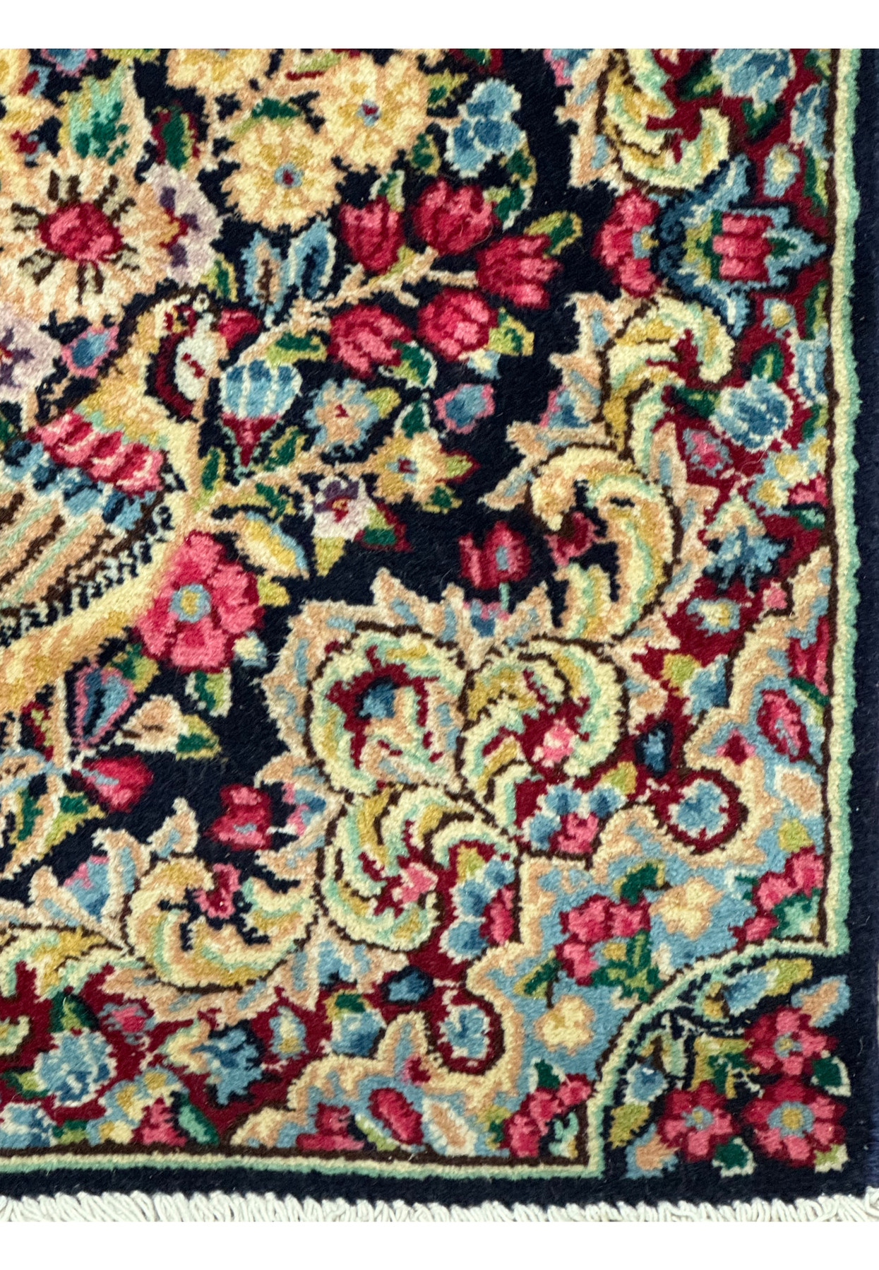 Corner section of a Persian Kerman rug showing the delicate fringe and border design
