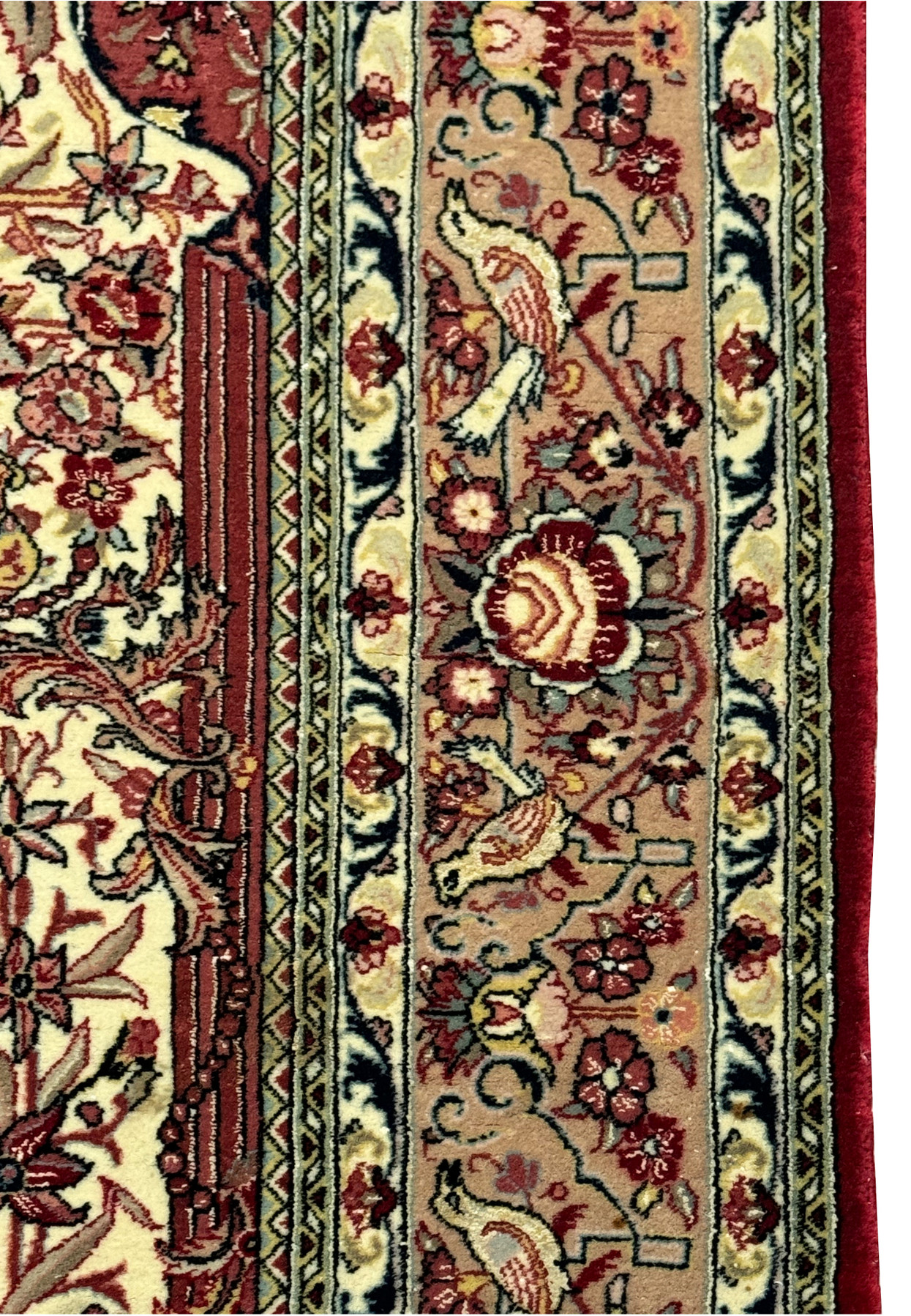 Close-up of the Persian Qum rug's border detailing, showing the precise patterns of florals and vines, and the subtle sheen of silk threads on the ornate background.
