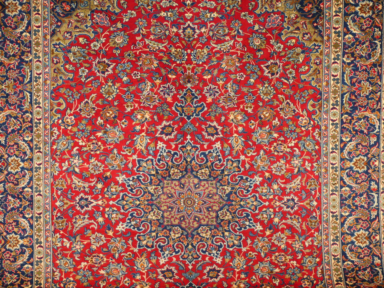 Close-up perspective of the Persian Isfahan rug's midfield, showcasing the central medallion's complex design, surrounded by a lush field of intertwined floral patterns in shades of blue, gold, and cream