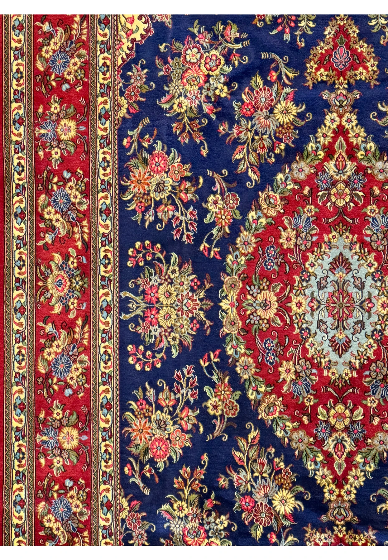 Detailed view of the edge and border of a Persian Qum Kork rug, featuring intricate floral and geometric patterns in red, cream, and gold on a contrasting navy background
