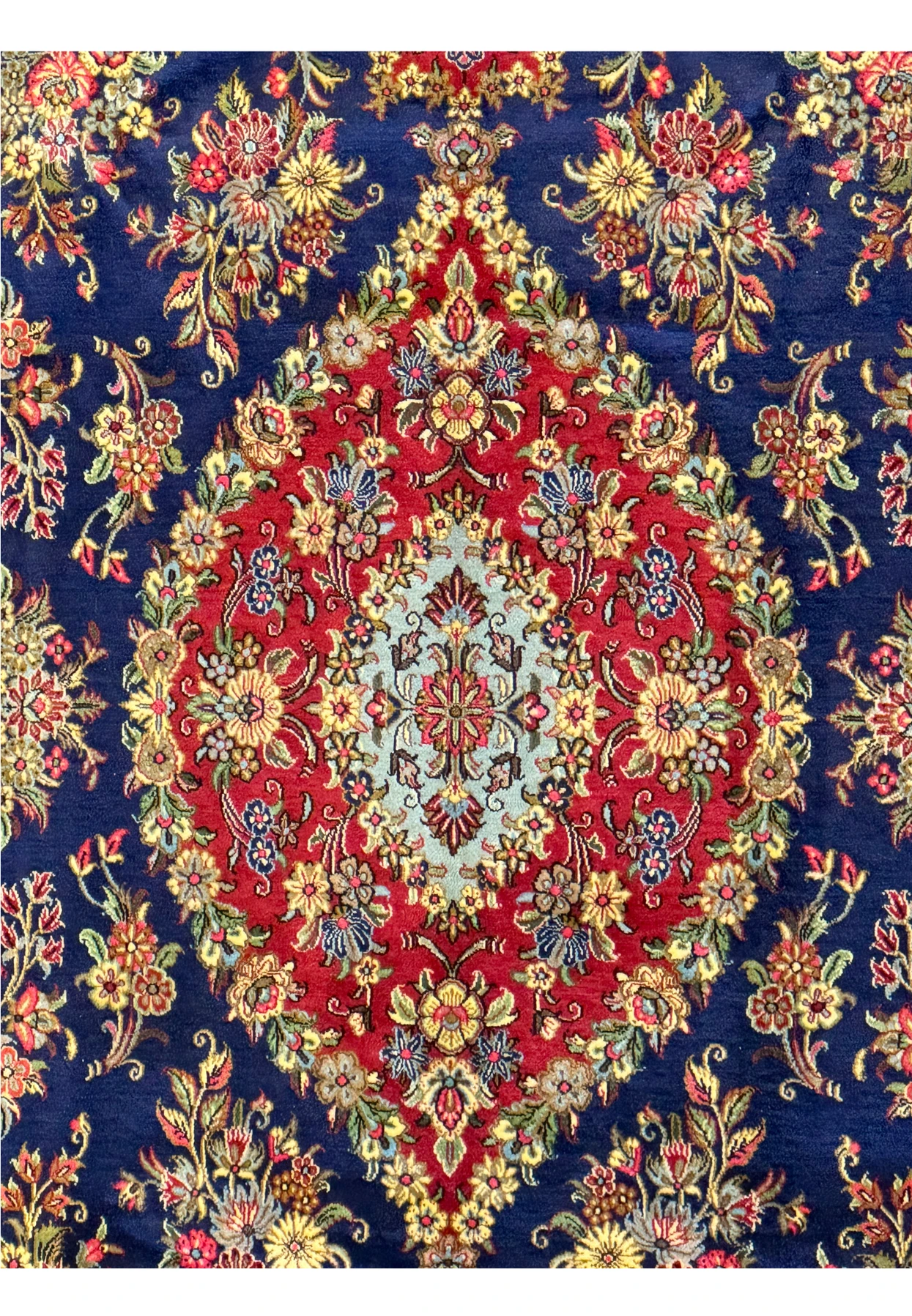 Close-up view of the central medallion on a Persian Qum Kork rug, detailed in red and cream with a complex array of floral designs and ornate patterns against a navy blue background