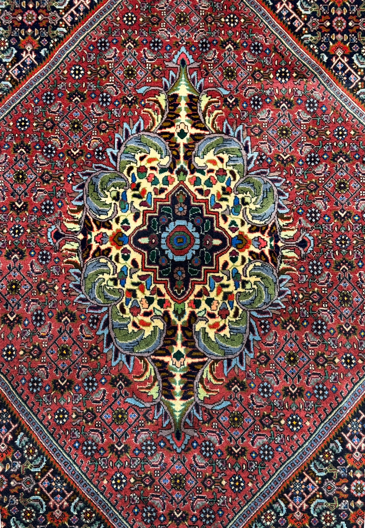 Close-up of the central medallion on the Persian Bidjar rug: A detailed close-up of the central medallion on the Persian Bidjar rug, revealing the intricate floral and geometric patterns in rich hues of red, yellow, green, blue, and black.