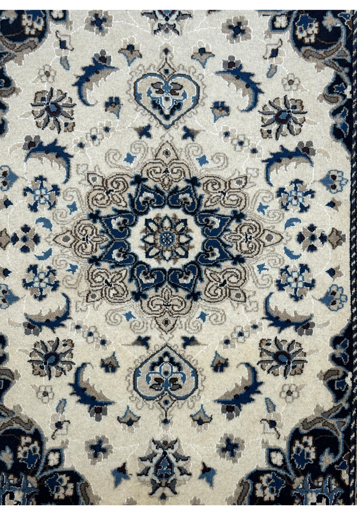 Close-up of the central medallion on a Nain Persian rug, featuring fine details in blue, beige, and ivory with floral accents.