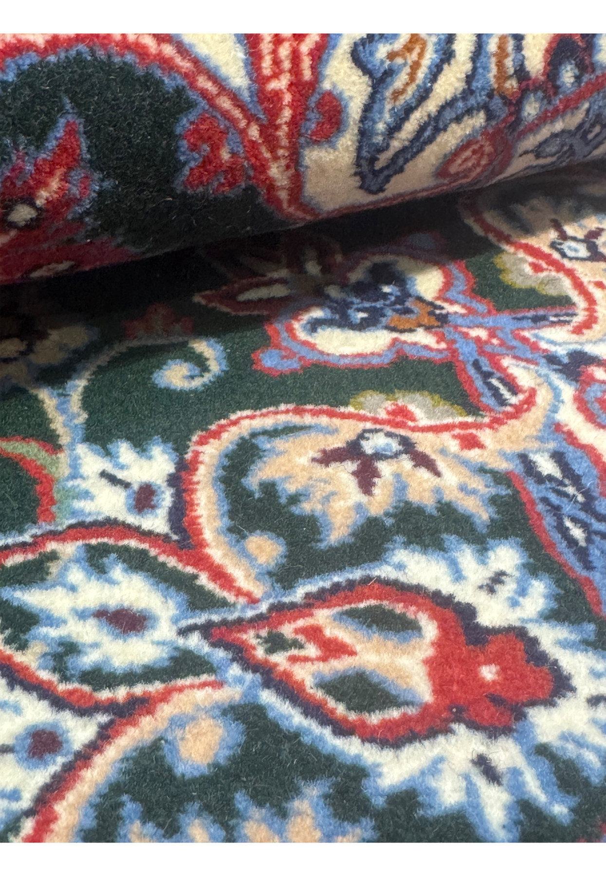 Rolled view of signed Persian Isfahan Seirafian wool and silk rug highlighting fine knotting and vibrant floral patterns.